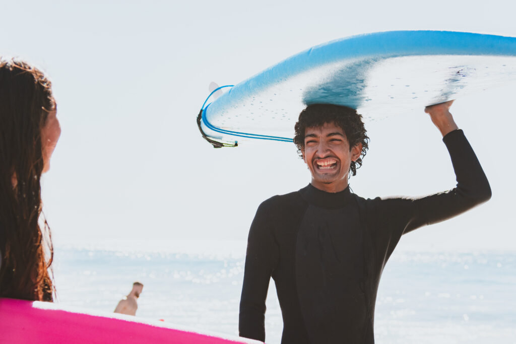 Chill youth smiling and balancing their surf board on their head.