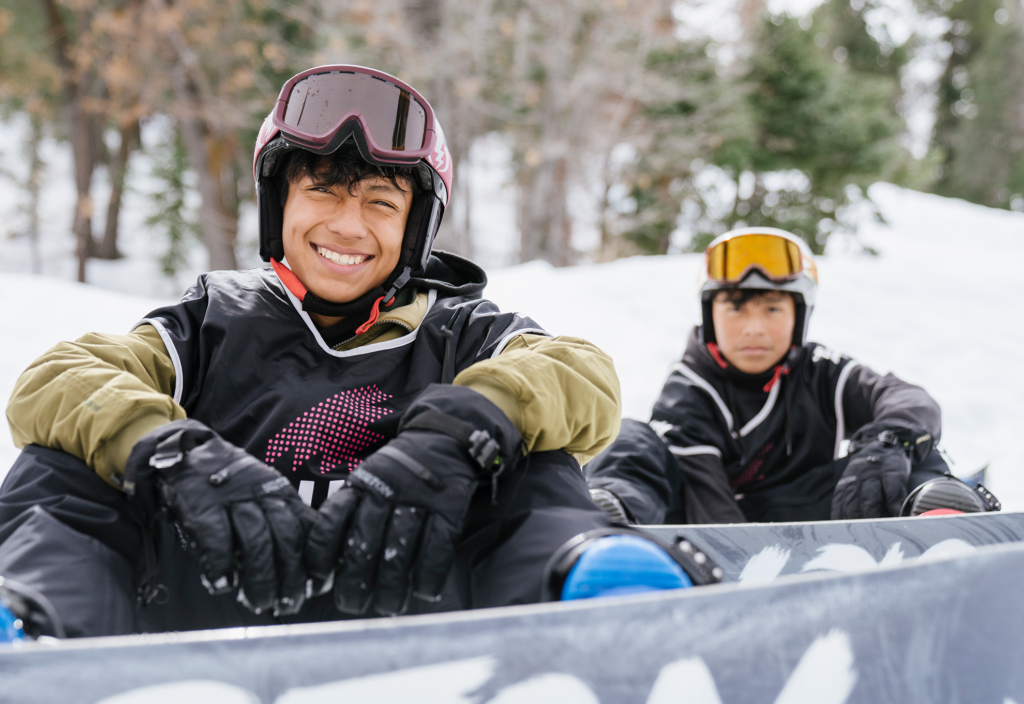 Two Chill snow participants smiling and sitting on the trail with their snowboards on.